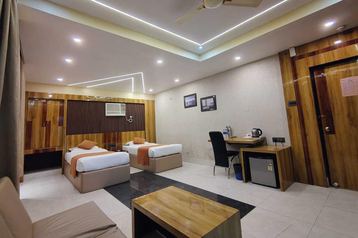 A hotel room with two beds, a desk, a chair, a small fridge, and a ceiling fan.