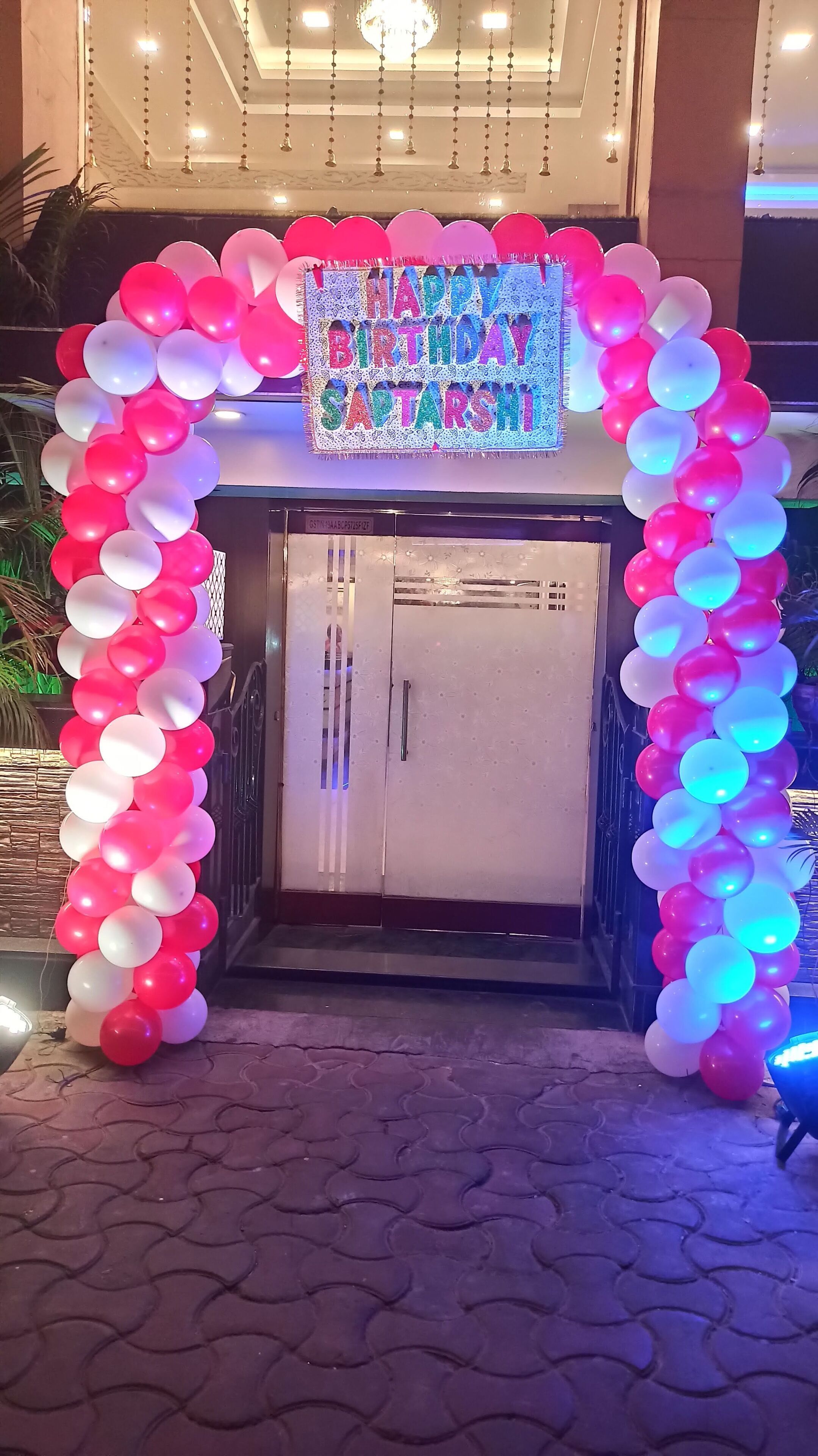 Uma porta adornada com um arco de balões coloridos e um letreiro com a mensagem 'Feliz Aniversário Captarshi'.