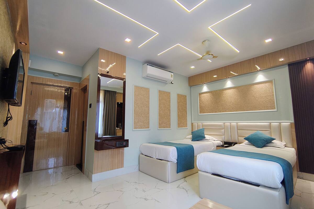 A hotel room with a modern design, including a large bed, a smaller bed, a vanity with a mirror, and a ceiling with recessed lighting.