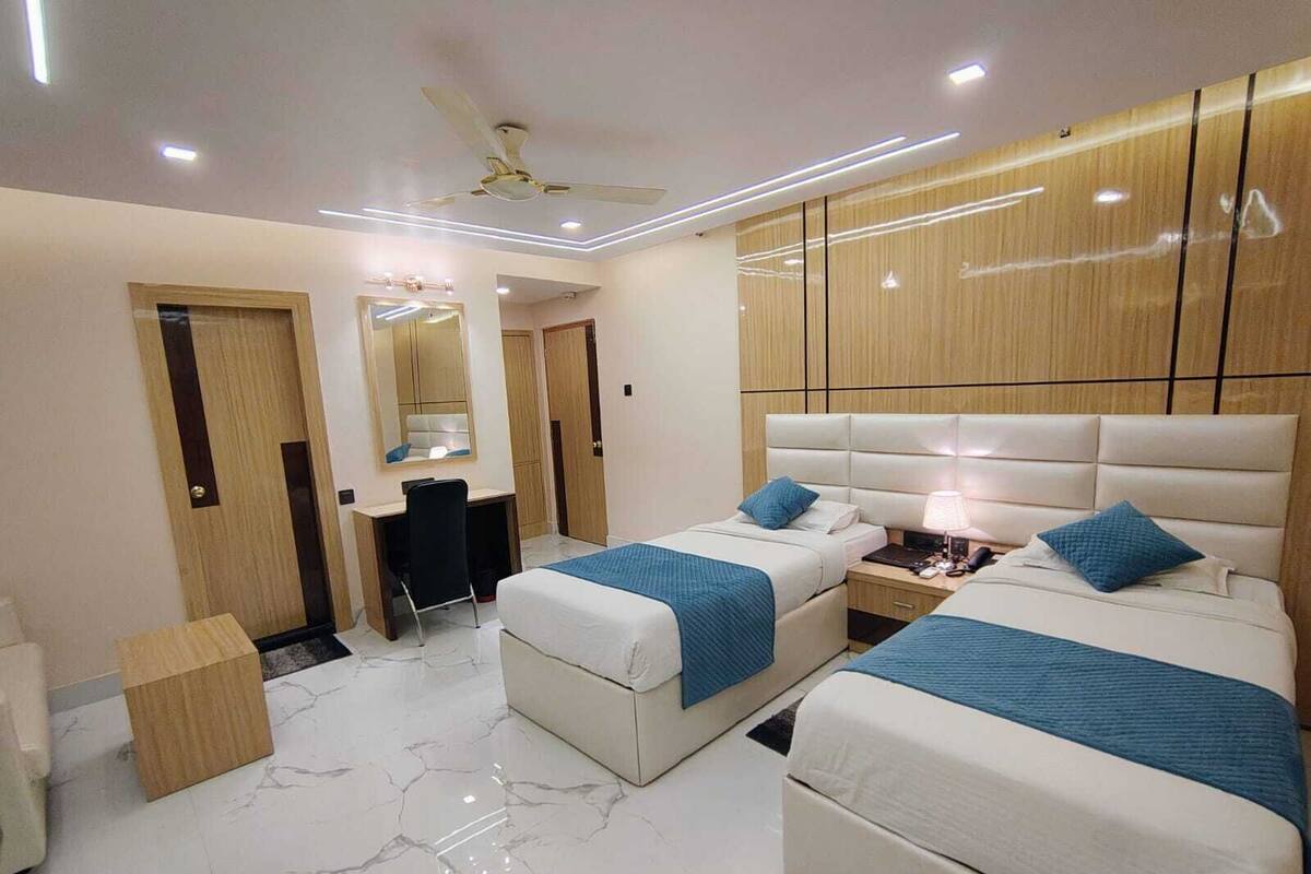 A hotel room with two beds, a desk, a chair, a mirror, and a ceiling fan.