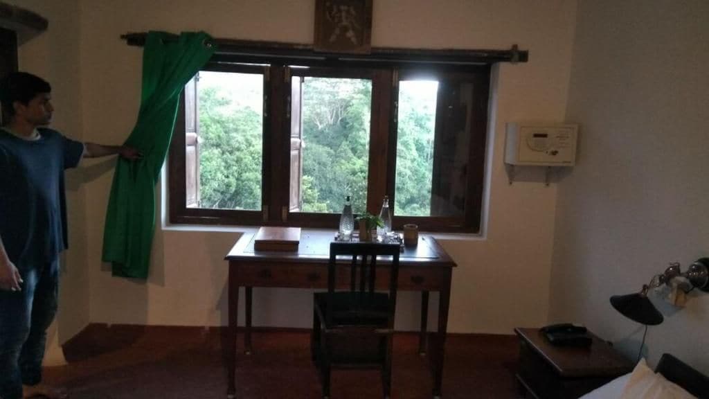 Ein Zimmer mit Schreibtisch, Stuhl und einem Vorhangfenster.