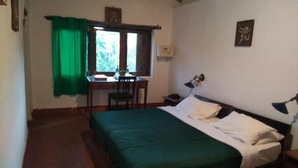 A room with a bed, a desk, and a chair. There is a window with curtains.