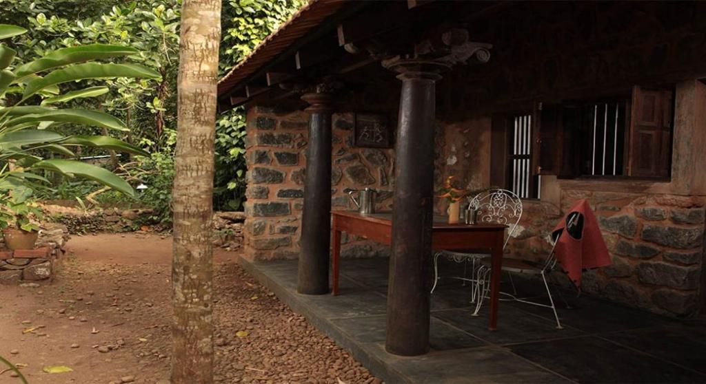 A rustic stone building with a covered porch, a table, and a chair.