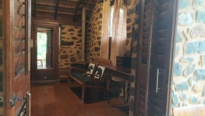 A rustic room with stone walls, wooden furniture, and a door leading outside. - Elephant Valley (Kodaikanal)