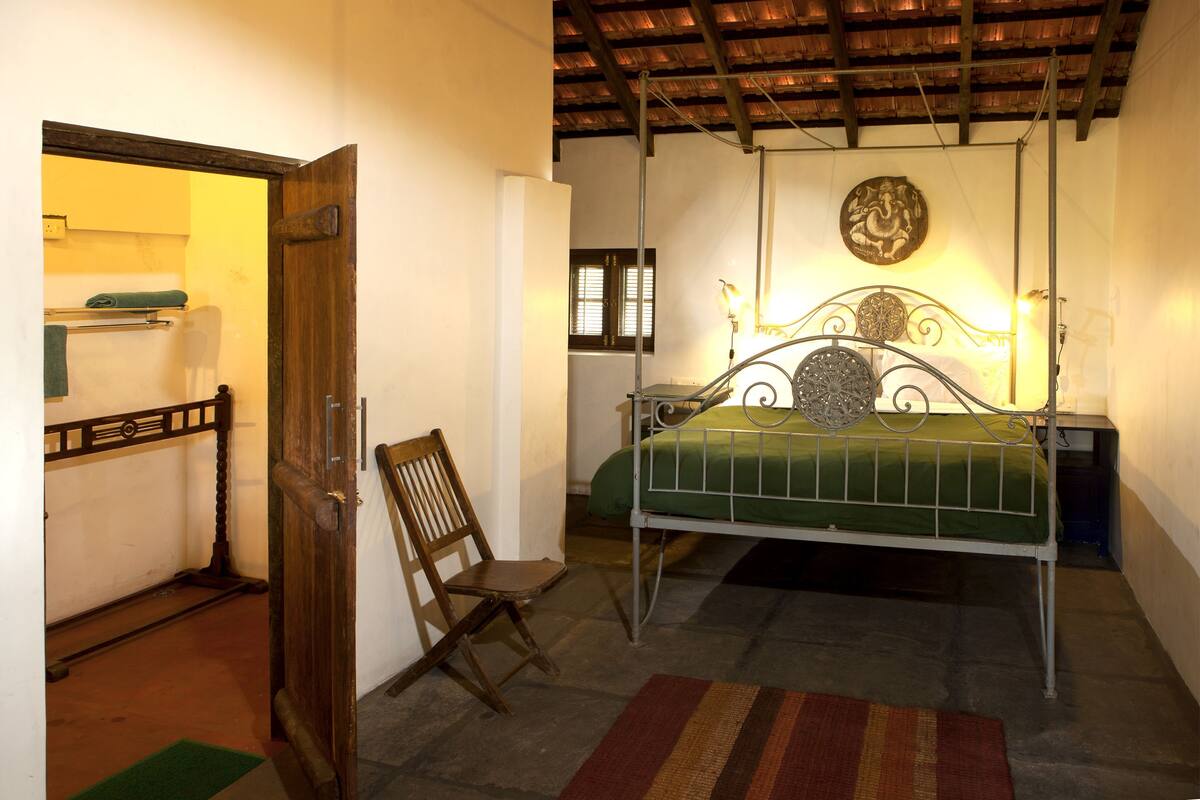 Un dormitorio con cama, una silla, una puerta de madera y una lámpara fijada a la pared.