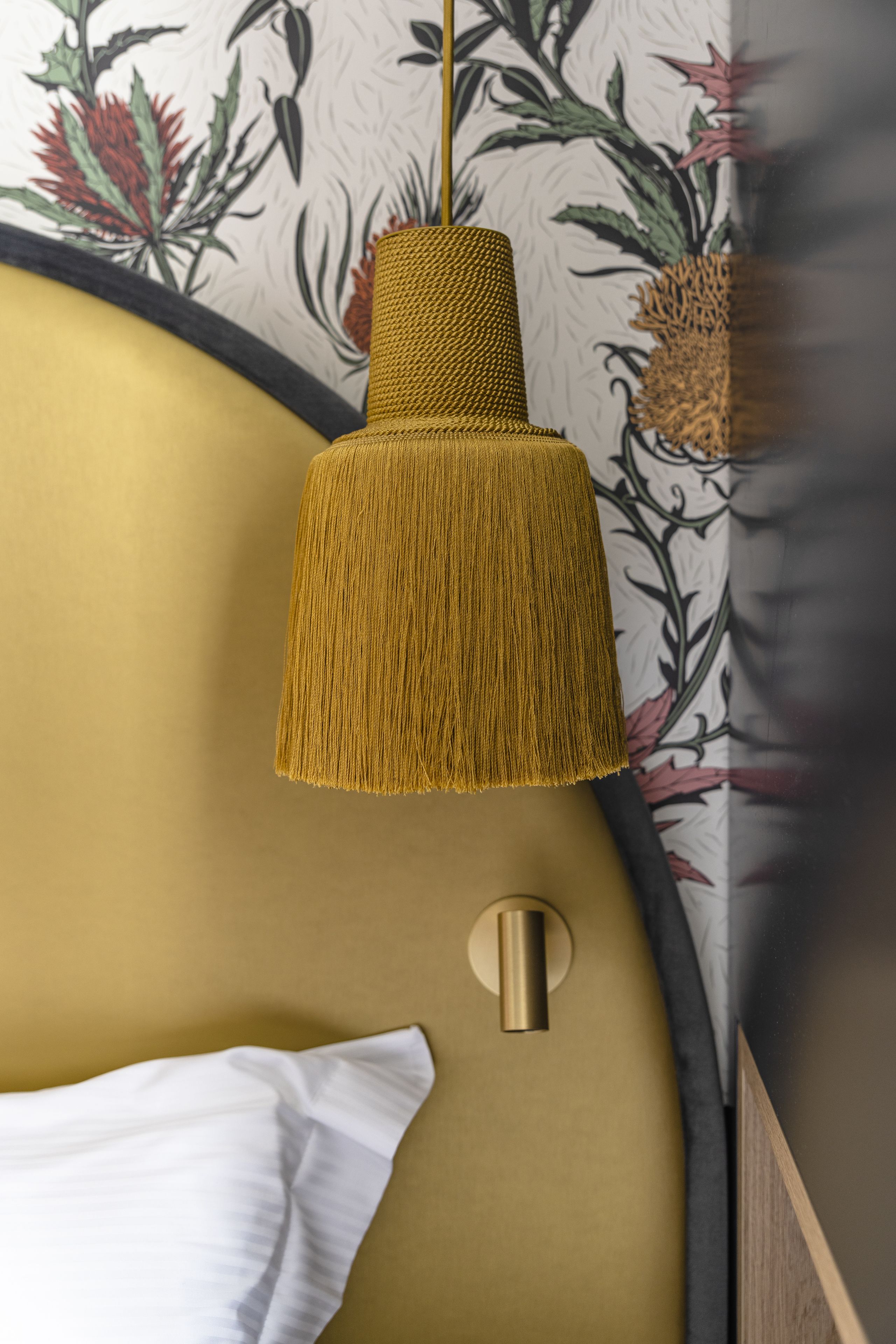Habitación con pared dorada, almohada blanca, lámpara colgante amarilla con textura y estampado de flores en el papel tapiz.