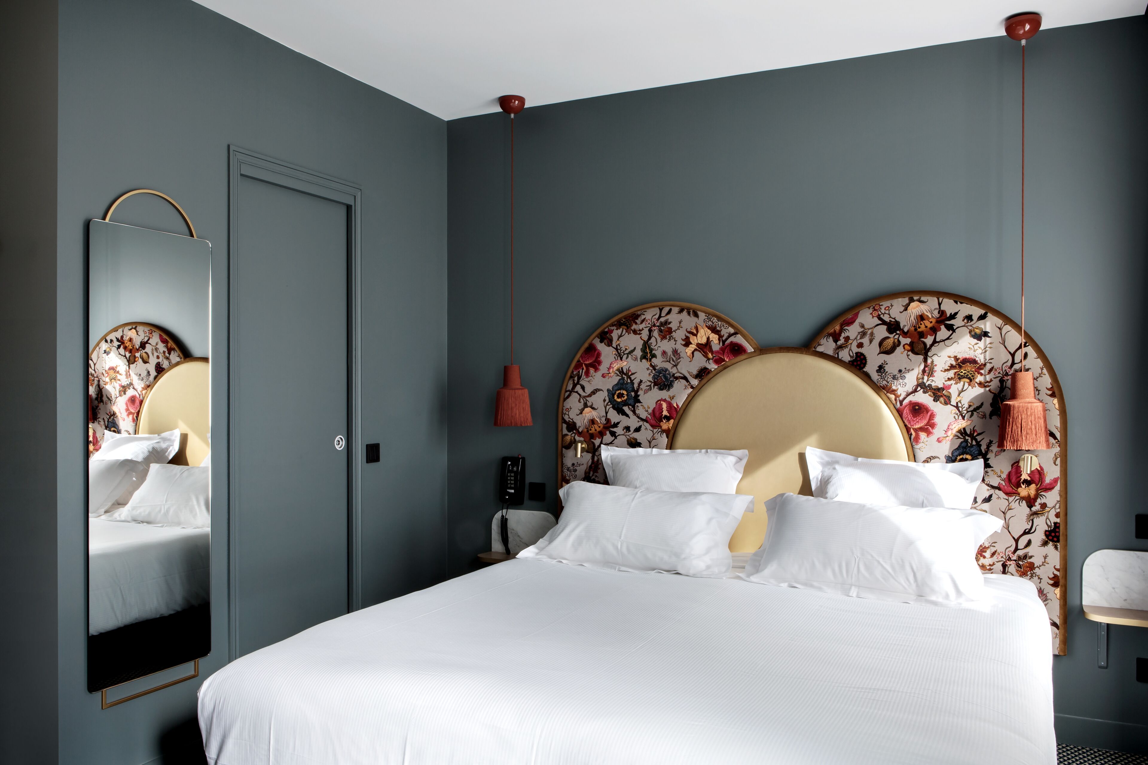 A neatly made bed with white linens, a floral headboard, and a wall-mounted telephone.