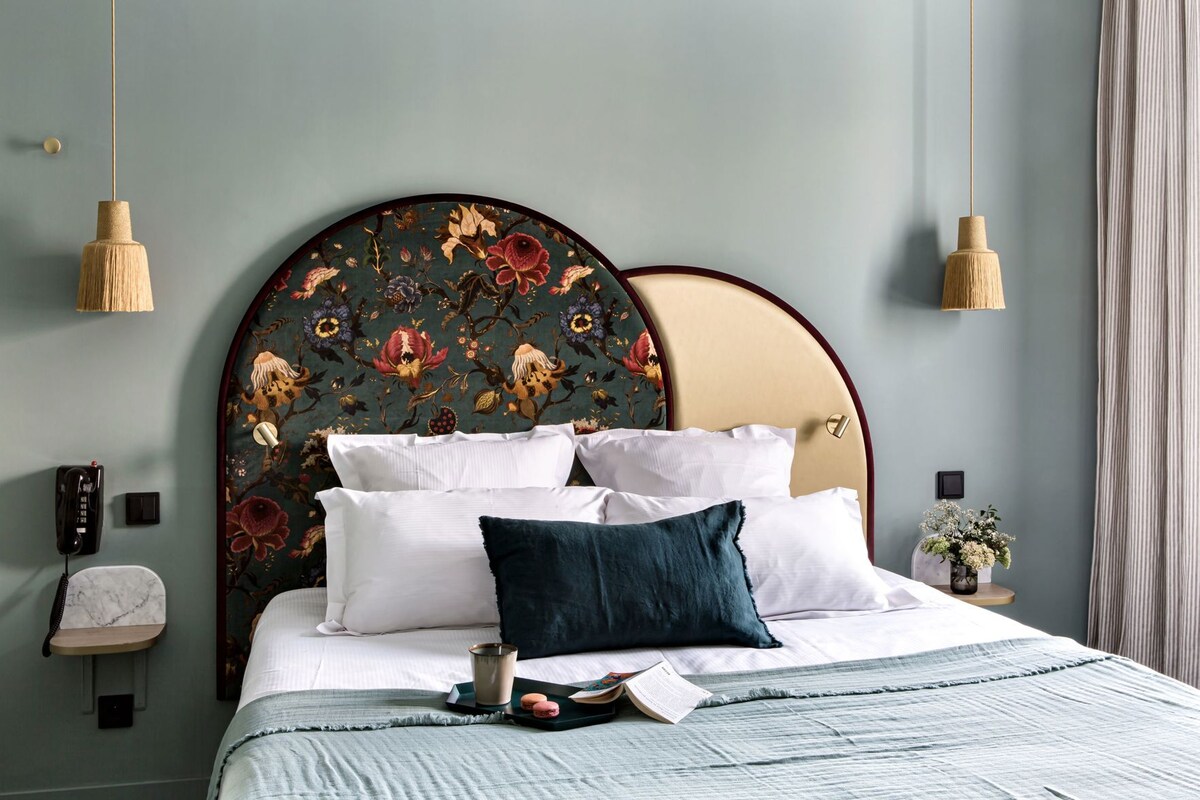 A bed with white and dark blue pillows, a bedside table with a vase of flowers, and a telephone on the wall.