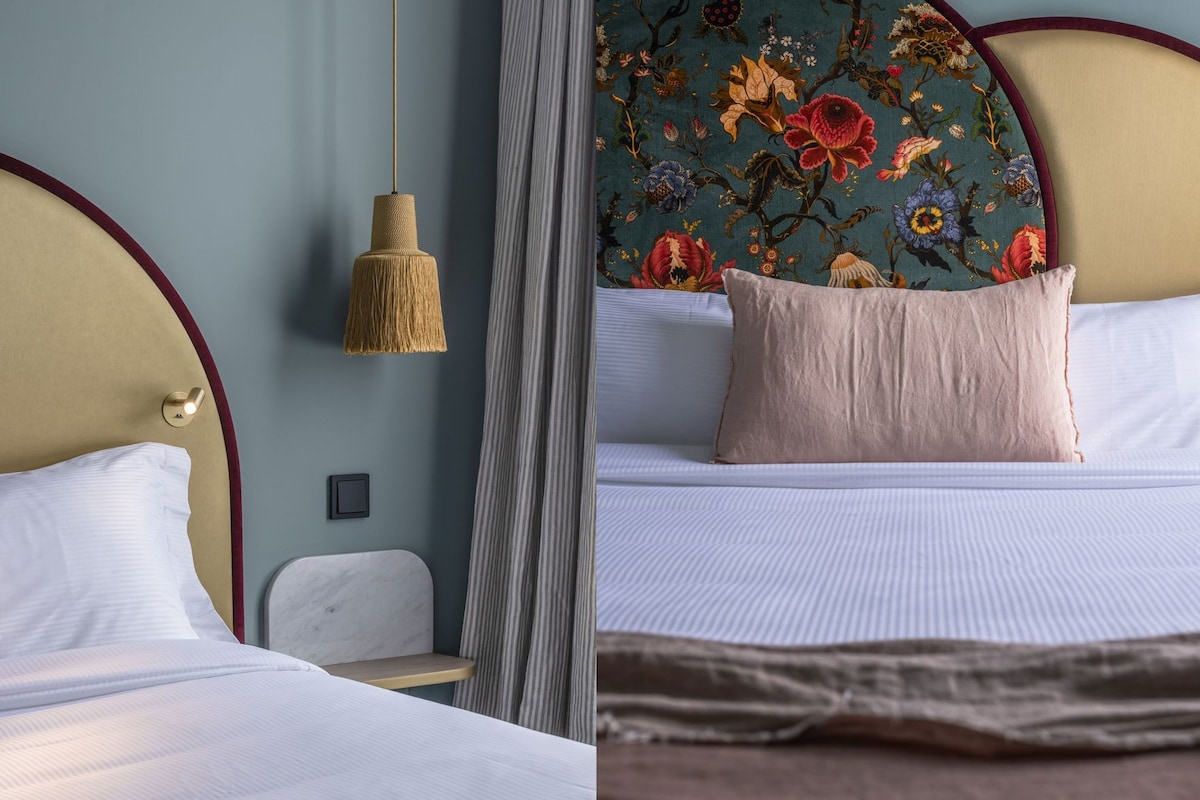 A bed with white linens, a hanging lamp, and a floral-patterned headboard.