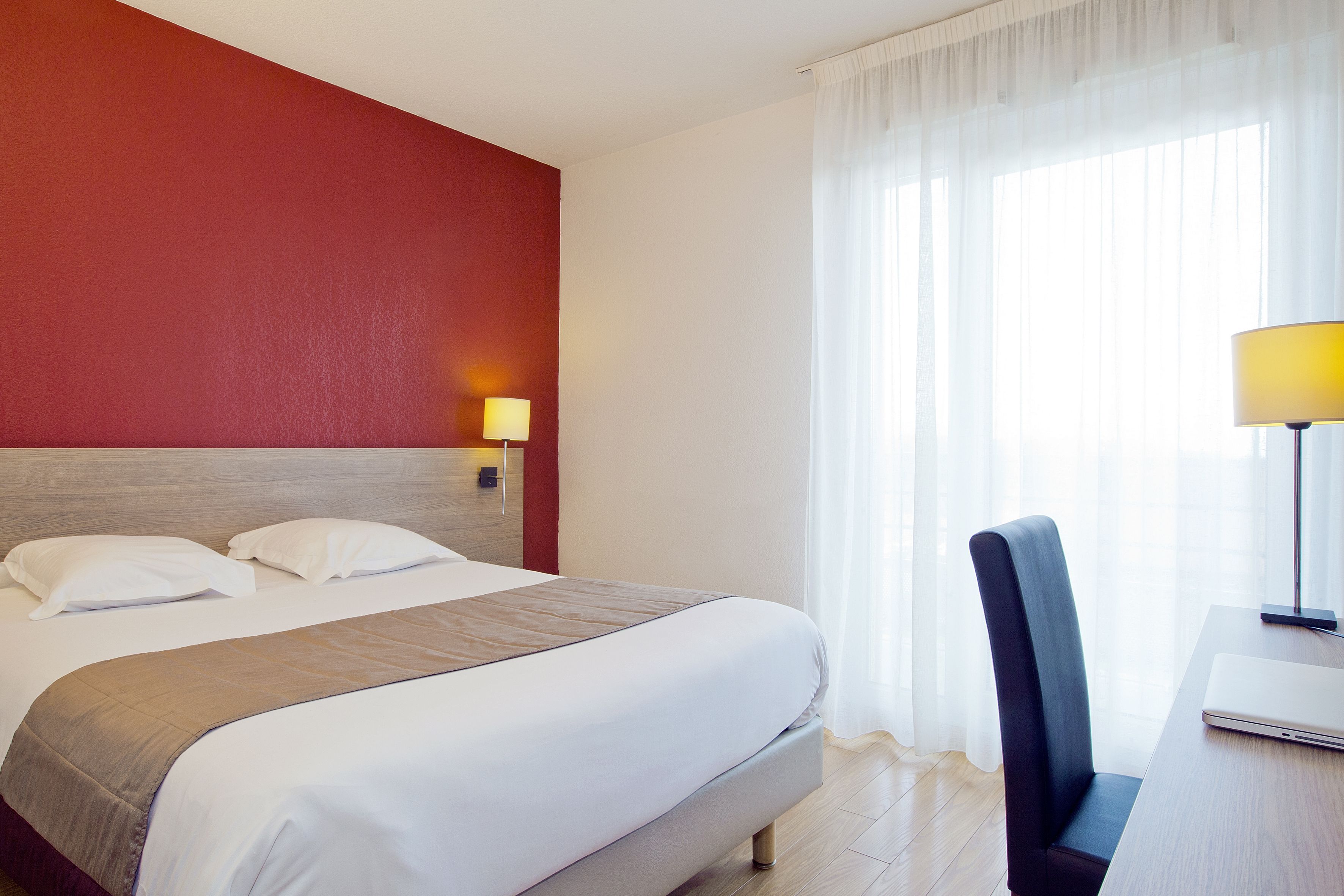 Een hotelkamer met een bed, een bureau met een laptop, een stoel en een lamp.