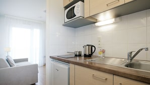 A modern kitchen with a built-in microwave, a kettle, and a sink. There is a small dishwasher and a sofa in the adjacent living area. - Séjours & Affaires Gex Les Rives du Leman (Gex)