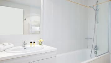 Un baño moderno con un tocador blanco, un espejo grande, una bañera y una ducha con mampara de vidrio.