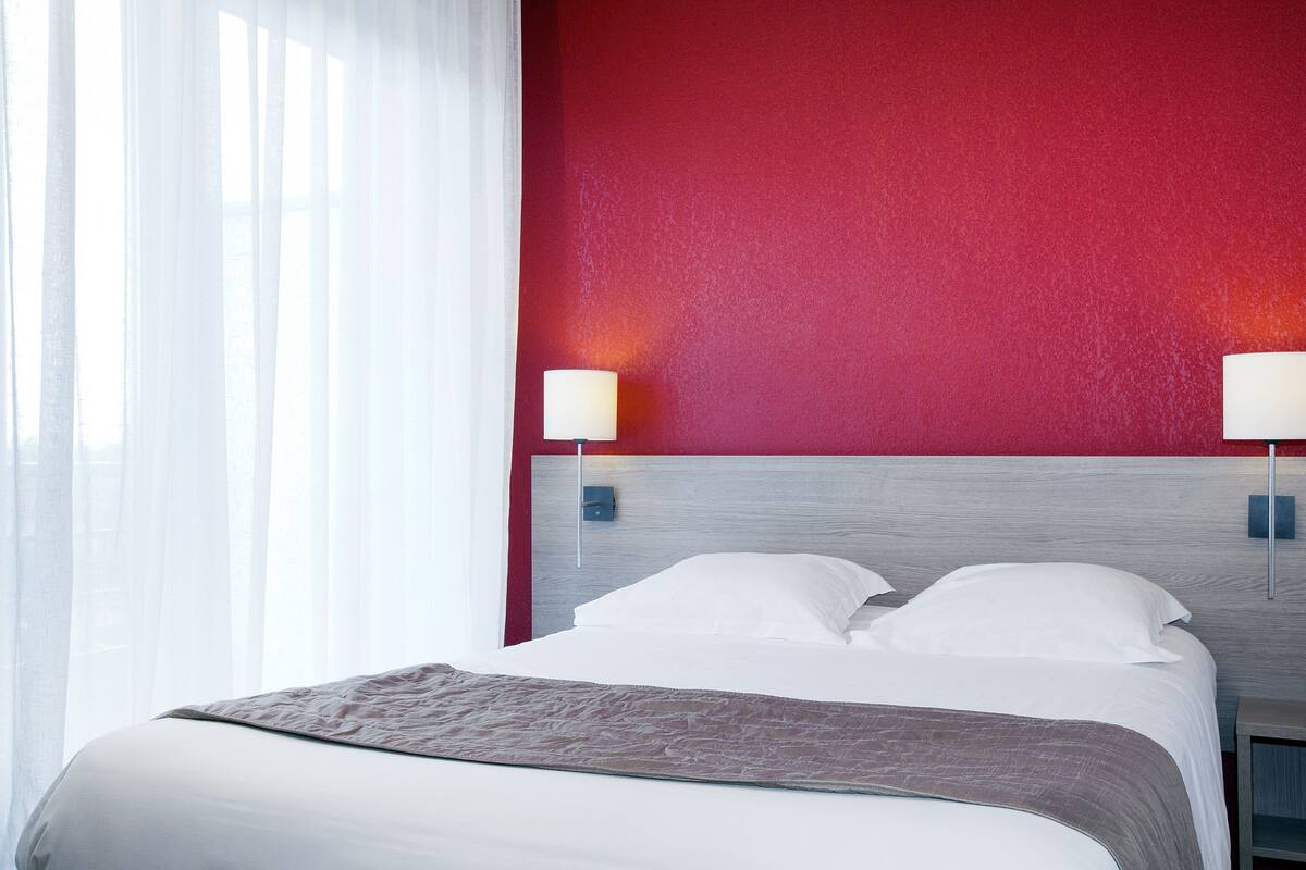 Una habitación de hotel con una cama, una pared decorada en rojo y dos lámparas de noche.