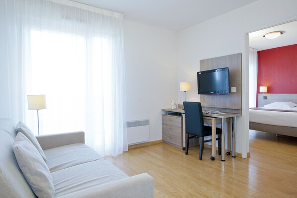 A modern hotel room with a bed, a desk with a computer, a TV, and a sofa.