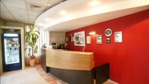 Un espace d’accueil avec un mur rouge, un comptoir en bois, des tableaux encadrés et une plante en pot.