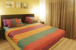 A bed with a colorful quilt, a wooden headboard, and a nightstand with a lamp. - Imperial Hotel (Tel Aviv)