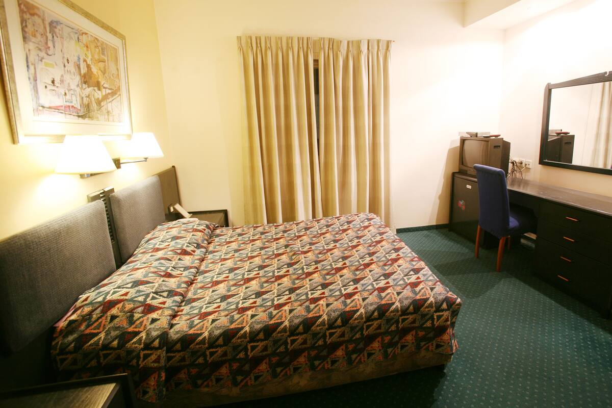Una habitación de hotel con una cama, un escritorio, una silla, un espejo y una lámpara.