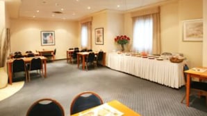 Une salle de conférence avec des tables et des chaises, une longue table recouverte d’une nappe blanche et une fenêtre avec des rideaux.