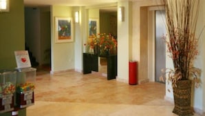 Un hall d’entrée avec un sol en marbre, un comptoir d’accueil, un vase rempli de fleurs et un panneau sur le mur.