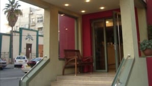 L’entrée d’un hôtel, avec une façade rouge et blanche, un escalier menant à l’entrée et une enseigne sur laquelle on peut lire « IMPERIAL ».