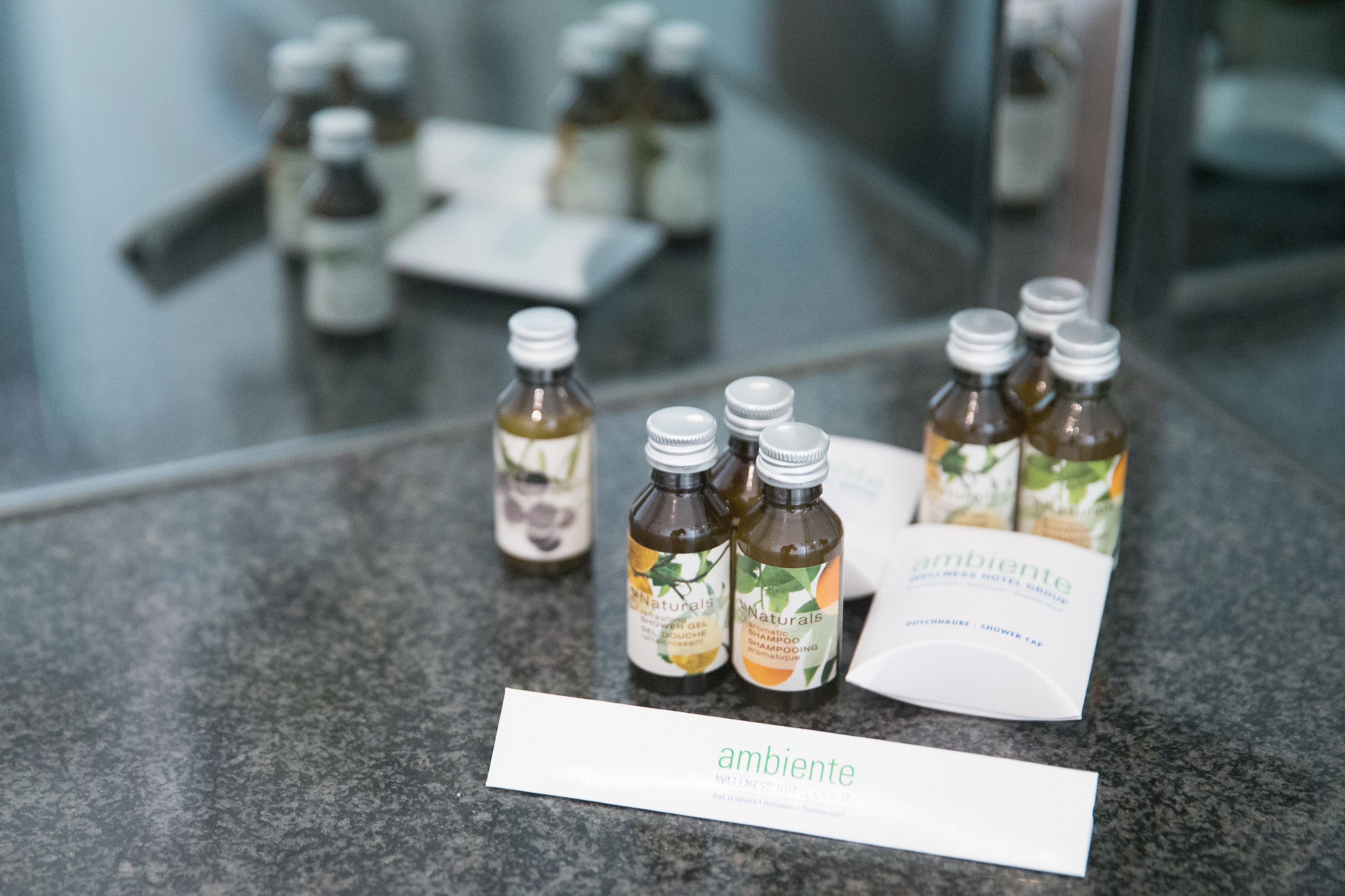 Una encimera de baño con botellas de gel de ducha y champú, un folleto y un cartel con la palabra 'ambiente'.