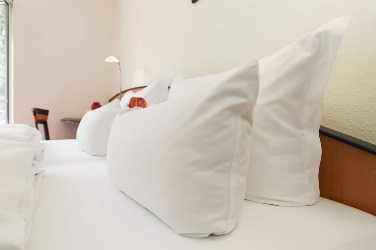 Habitación de hotel con una cama bien hecha, una silla, una lámpara y una lámpara de pared.