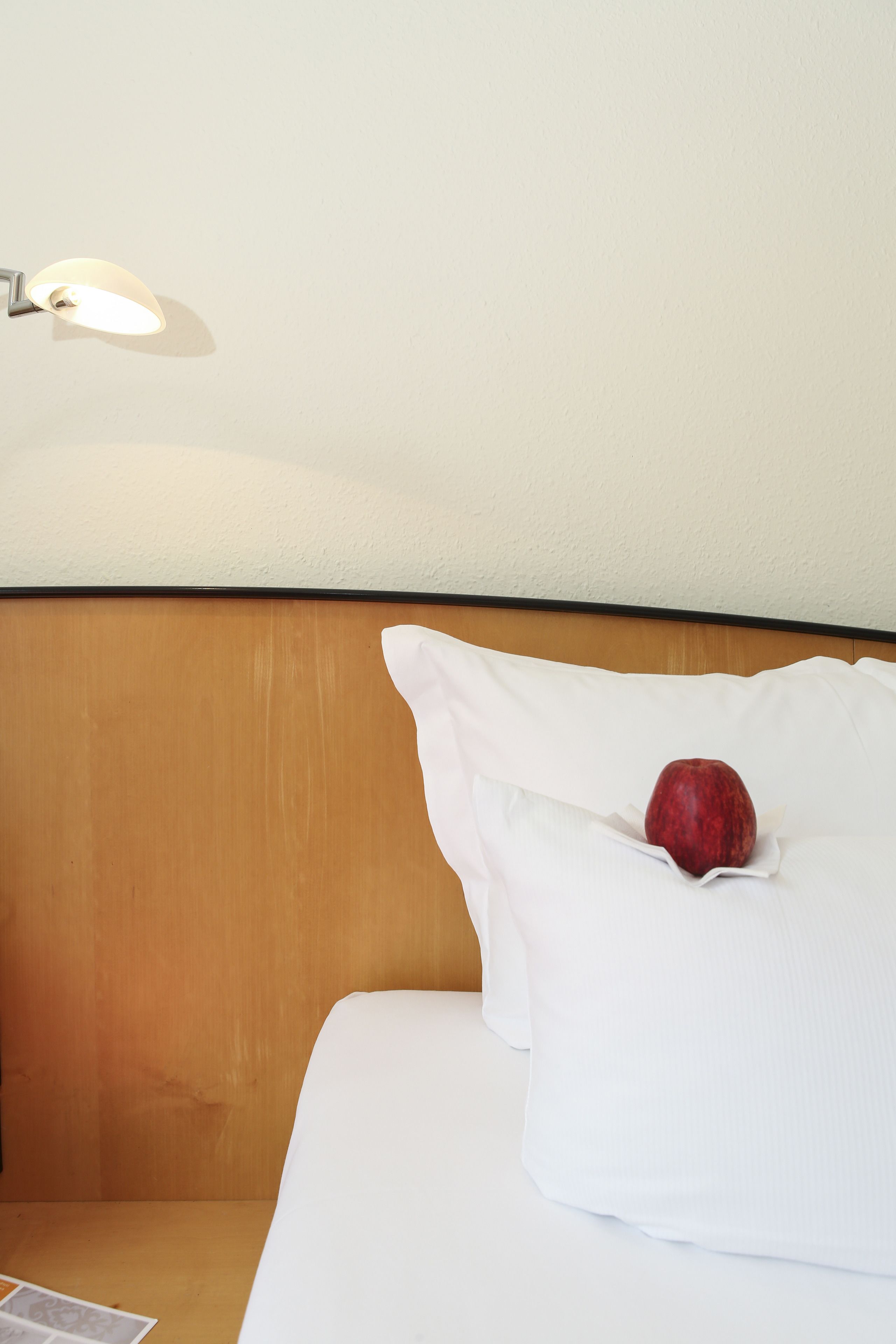 Habitación de hotel con cabecera de madera, ropa de cama blanca y una manzana roja sobre una almohada.
