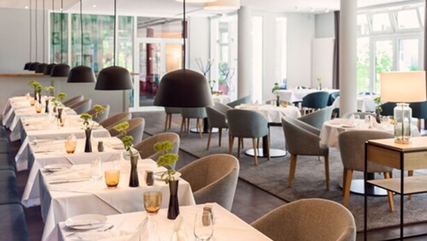 A modern restaurant with long tables, chairs, and pendant lighting. - VITALHOTEL ambiente (Bad Wilsnack)