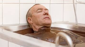 A person in a bathtub with water running from a faucet.