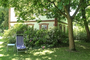 A garden with a chair and table, a tree, and a building with a brick facade. - VITALHOTEL ambiente (Bad Wilsnack)