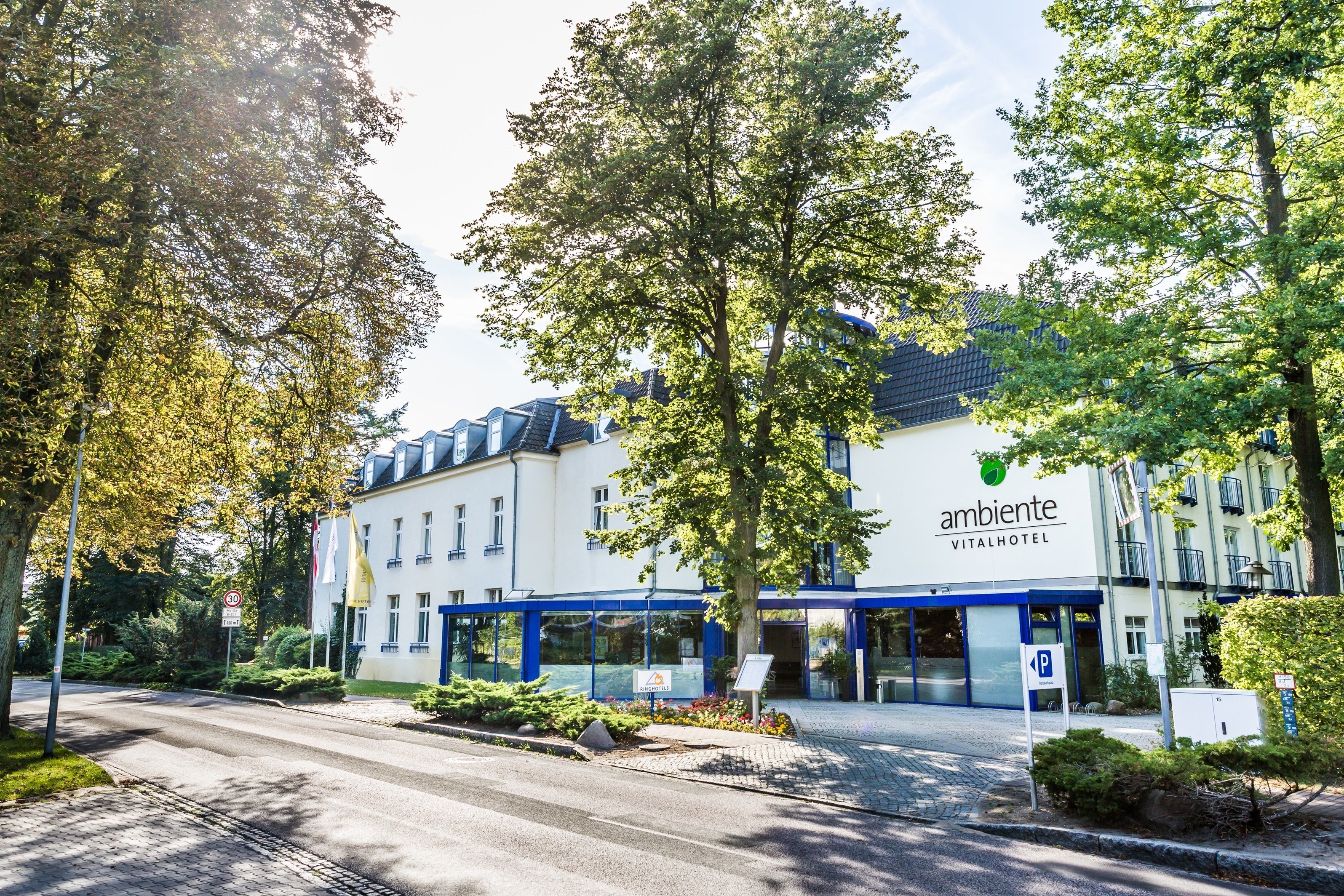A hotel with a modern design, featuring a prominent 'ambiente vital hotel' sign, a covered entrance, and a parking area.