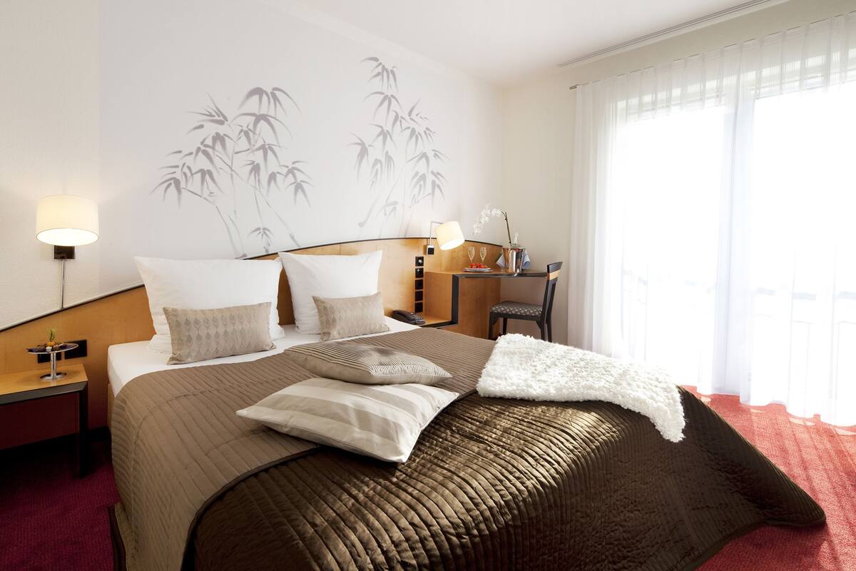 Una habitación de hotel con una cama grande, una mesita de noche, un escritorio y una silla.
