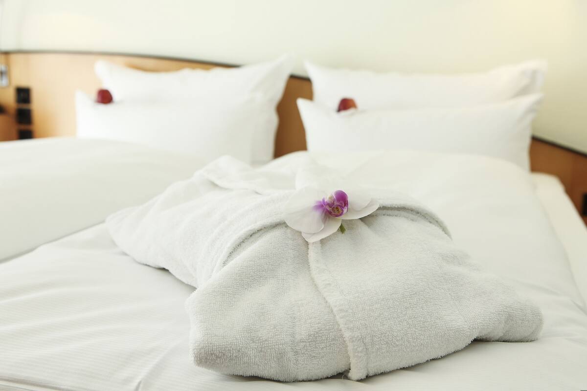 Una cama bien hecha con sábanas blancas y una sola flor morada.