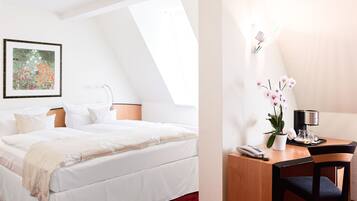 Habitación de hotel con cama, escritorio con silla, teléfono, cafetera y una orquídea en maceta.