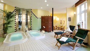 A spa area with two hot tubs, a wooden partition, and a seating area with chairs. - VITALHOTEL ambiente (Bad Wilsnack)
