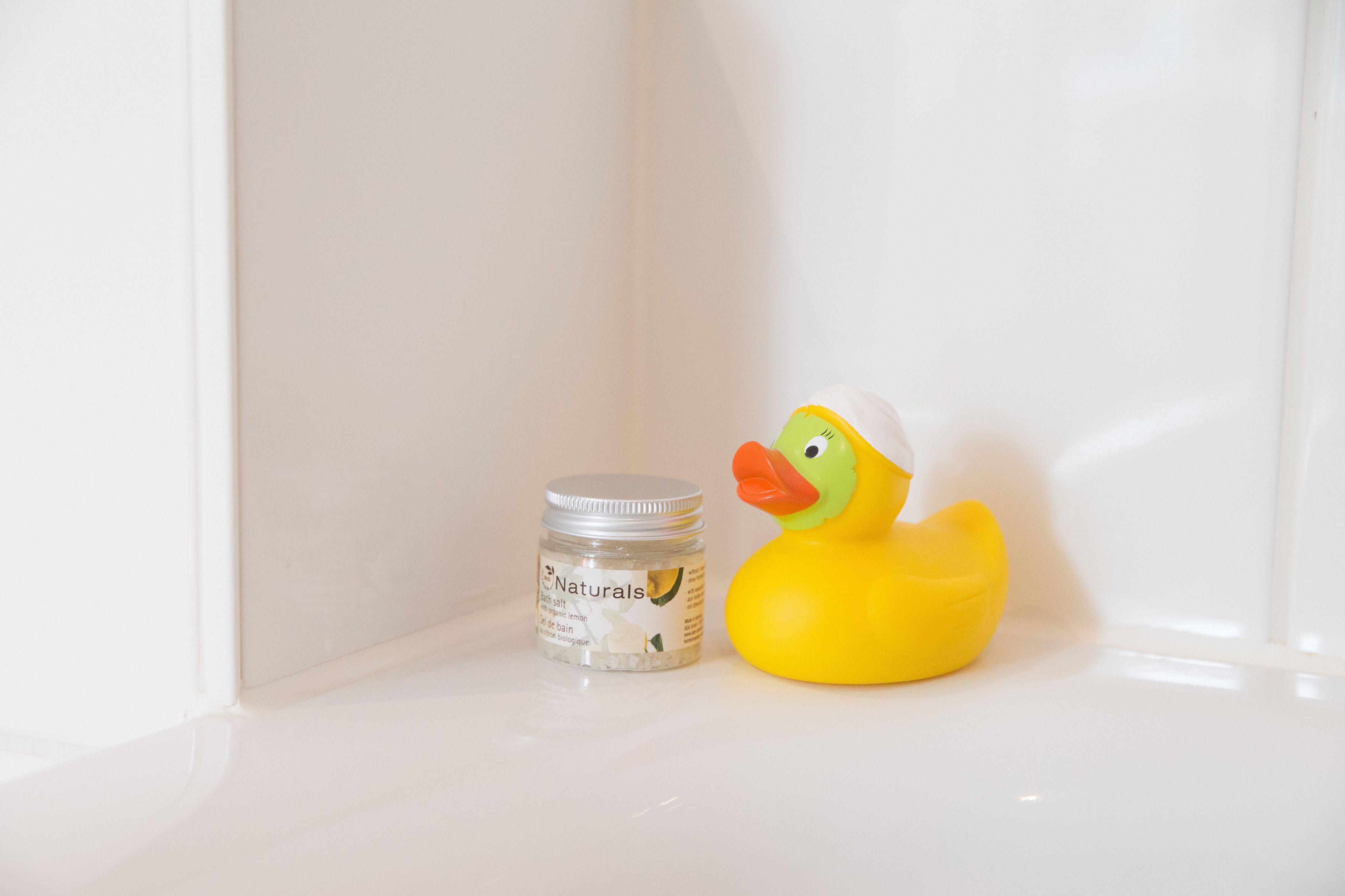 Eine kleine Flasche Naturals Babyöl neben einem gelben Gummiente in einer Ecke.