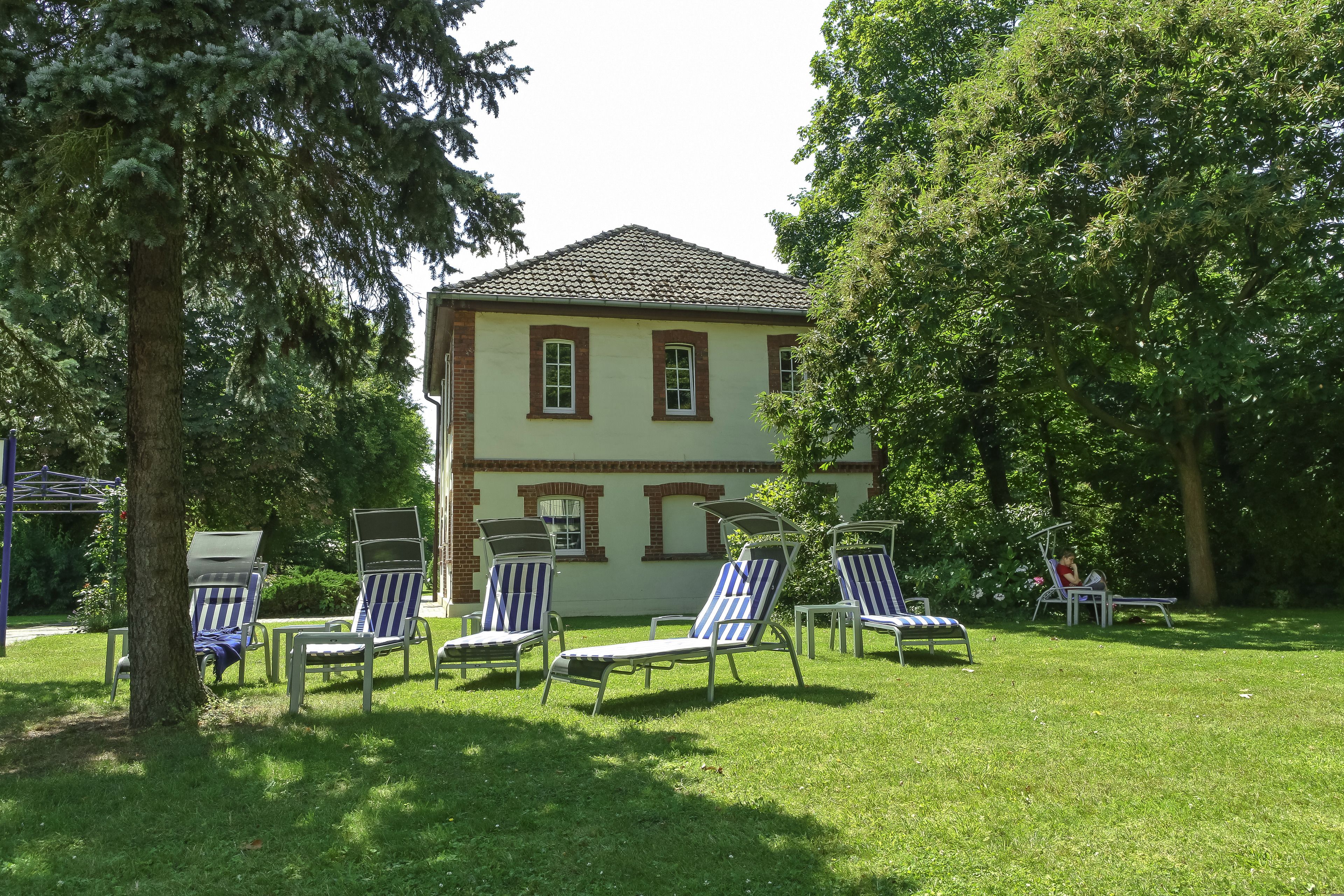 A building with a tiled roof and a brick facade, surrounded by a grassy lawn with several lounge chairs.