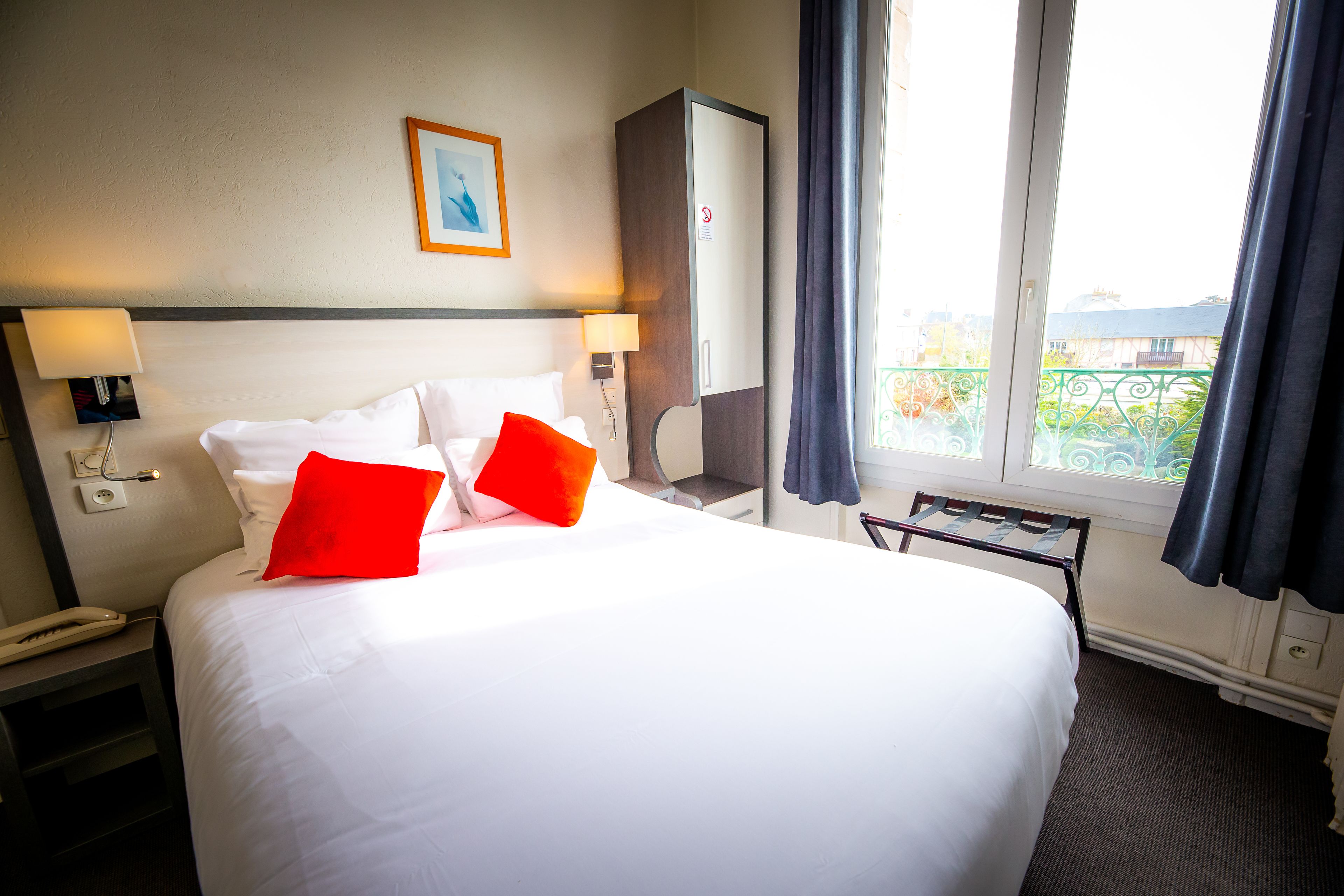 Una habitación de hotel con una cama grande, dos lámparas de noche, un escritorio con una silla, un armario y una ventana con cortinas.