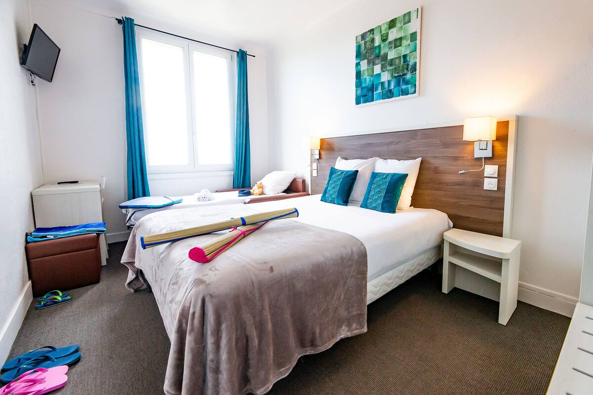 A hotel room with a bed, bedside table, nightstand, and a television on the wall.