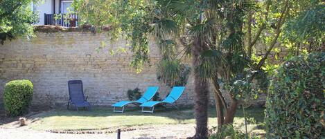 A courtyard with a stone wall, two blue lounge chairs, and a palm tree.
