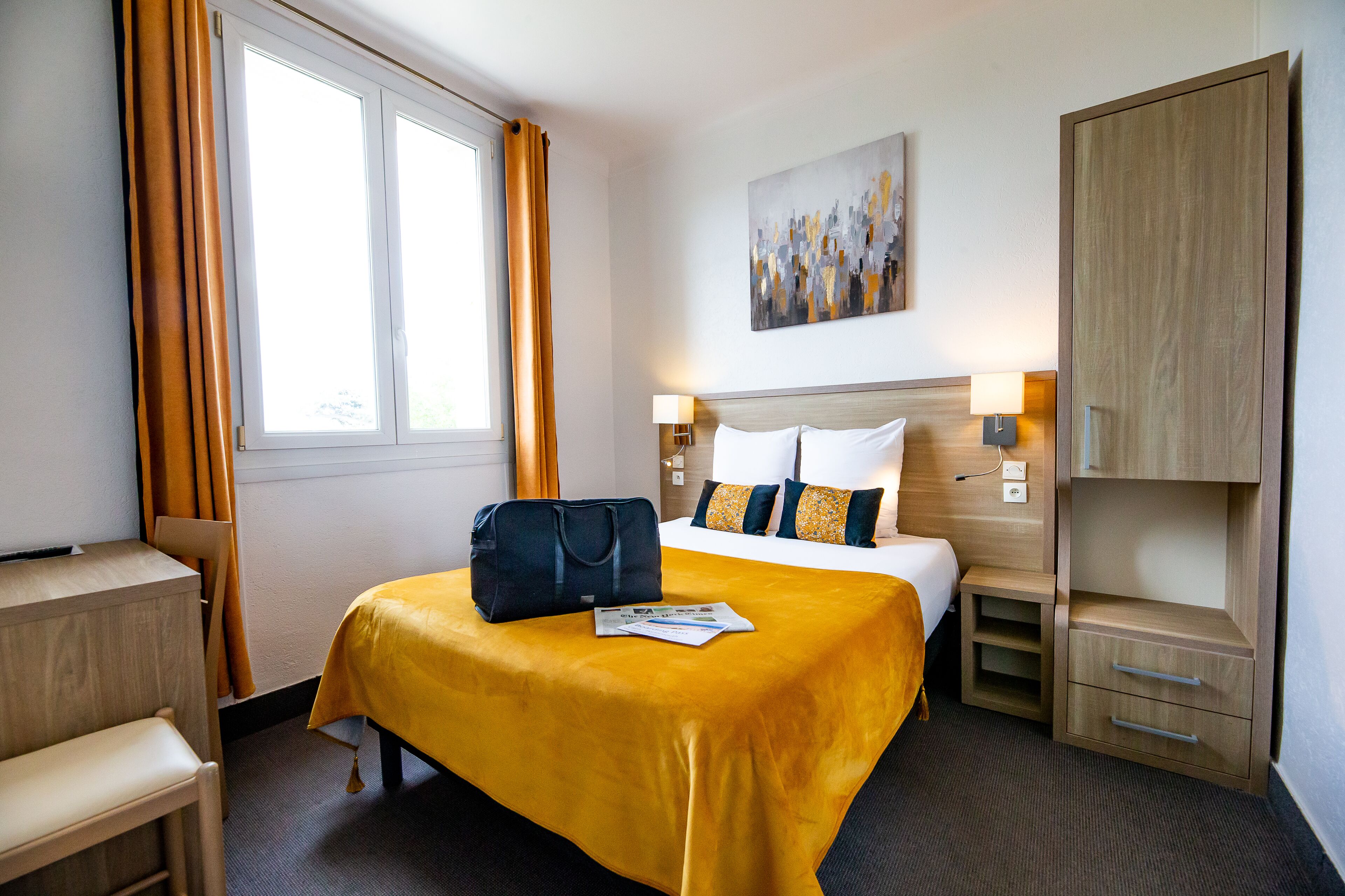 A hotel room with a bed, a desk, a chair, a wardrobe, and a window with curtains.