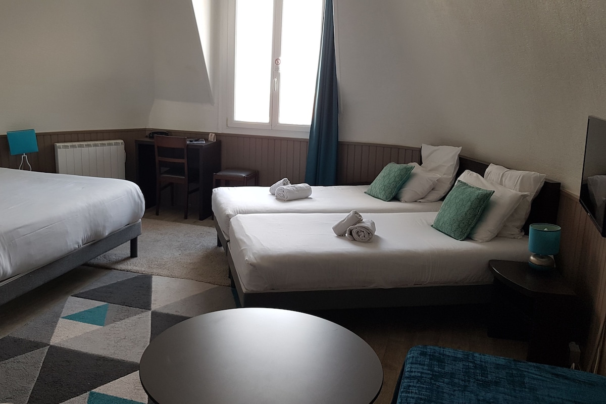 Habitación de hotel con dos camas, un escritorio, una silla, una mesa redonda y una ventana con cortinas.