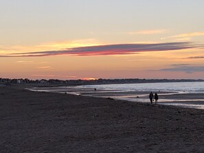 A beach at sunset with a distant shoreline and a few people walking along the water. - La Villa Andry (Ouistreham)