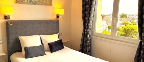 A hotel room with a bed, two wall-mounted lamps, a painting, and a window with curtains.