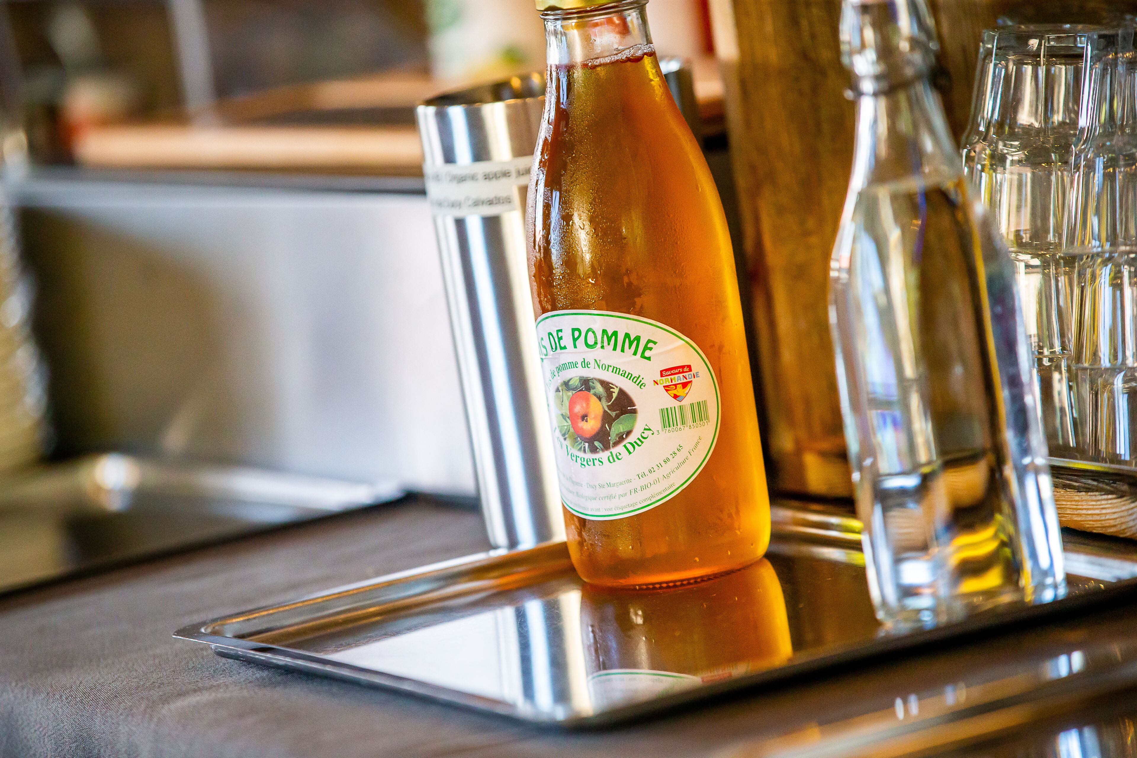 Une bouteille de cidre sur un plateau, accompagnée de verres et d’un récipient en métal.