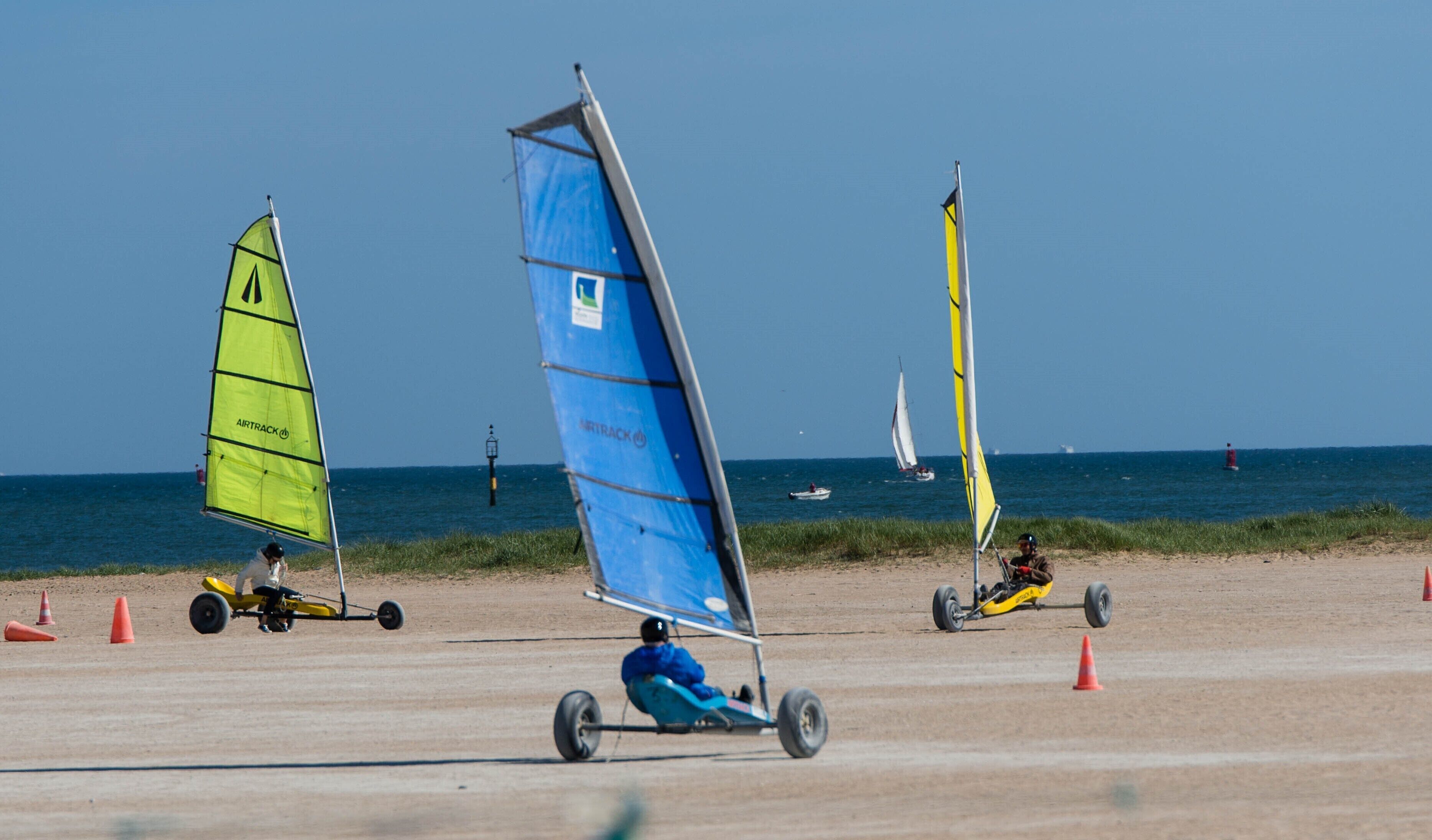 A beach with windsurfing equipment and a sailboat in the background.