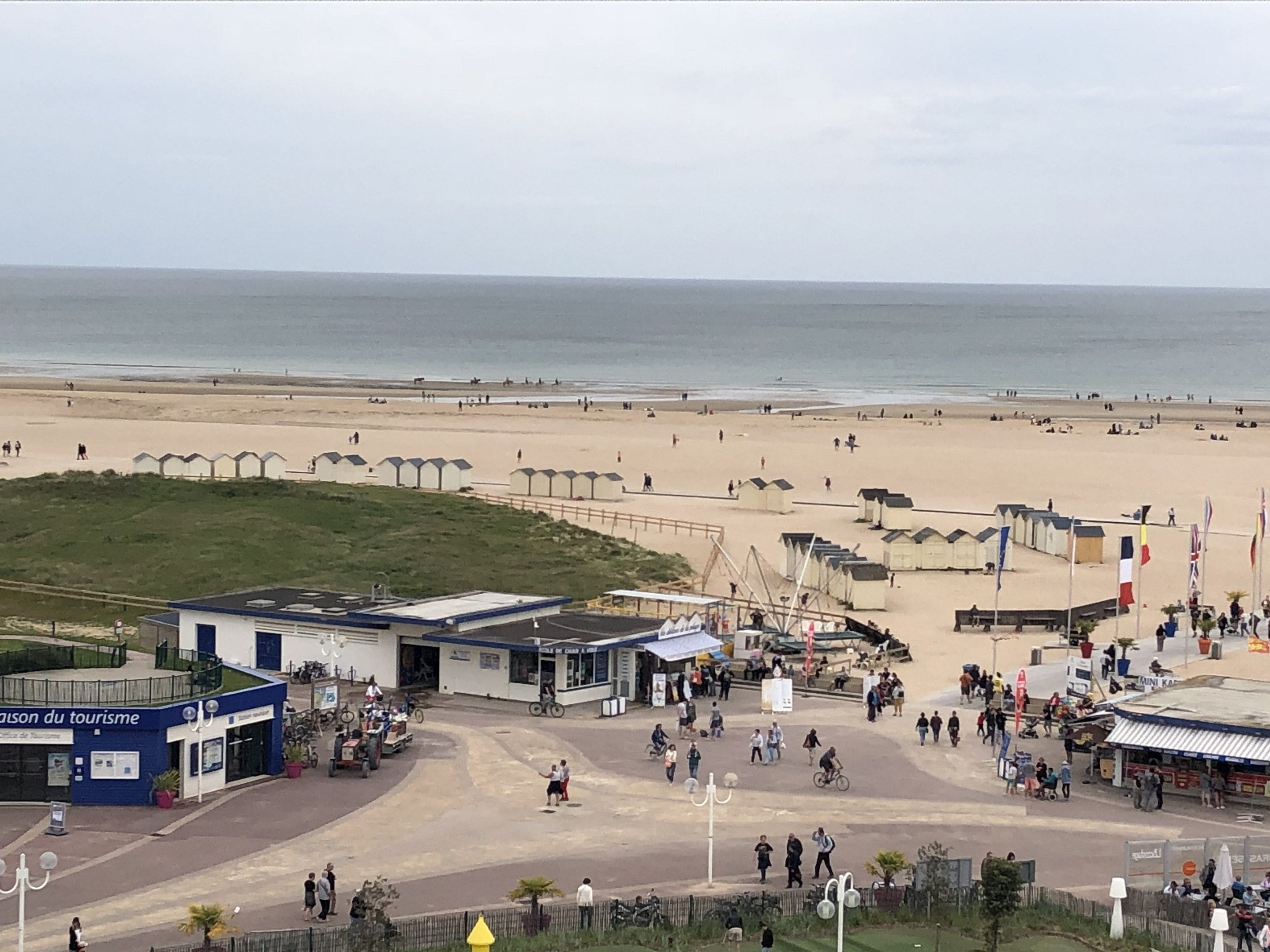 Ubicación junto a la playa con un edificio que dice 'Maison du Tourisme', arena, sombrillas y gente.