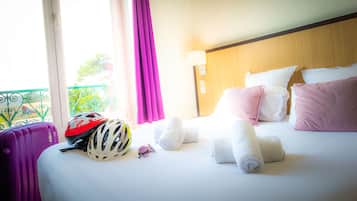 Habitación de hotel con cama, almohadas, cabecera, ventana con cortinas, maleta y casco.