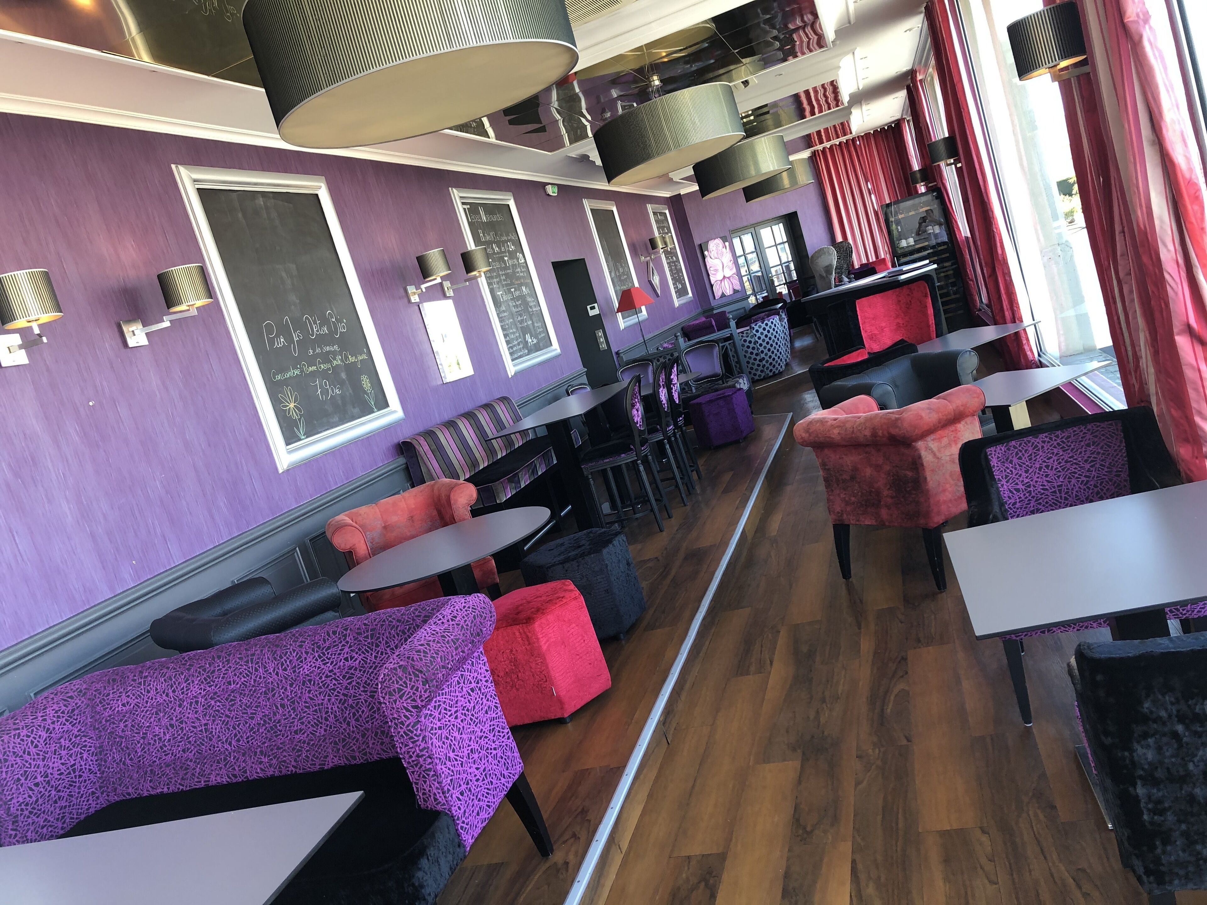 Interior de restaurante con paredes moradas, asientos tapizados en negro y rojo, y suelo de madera.
