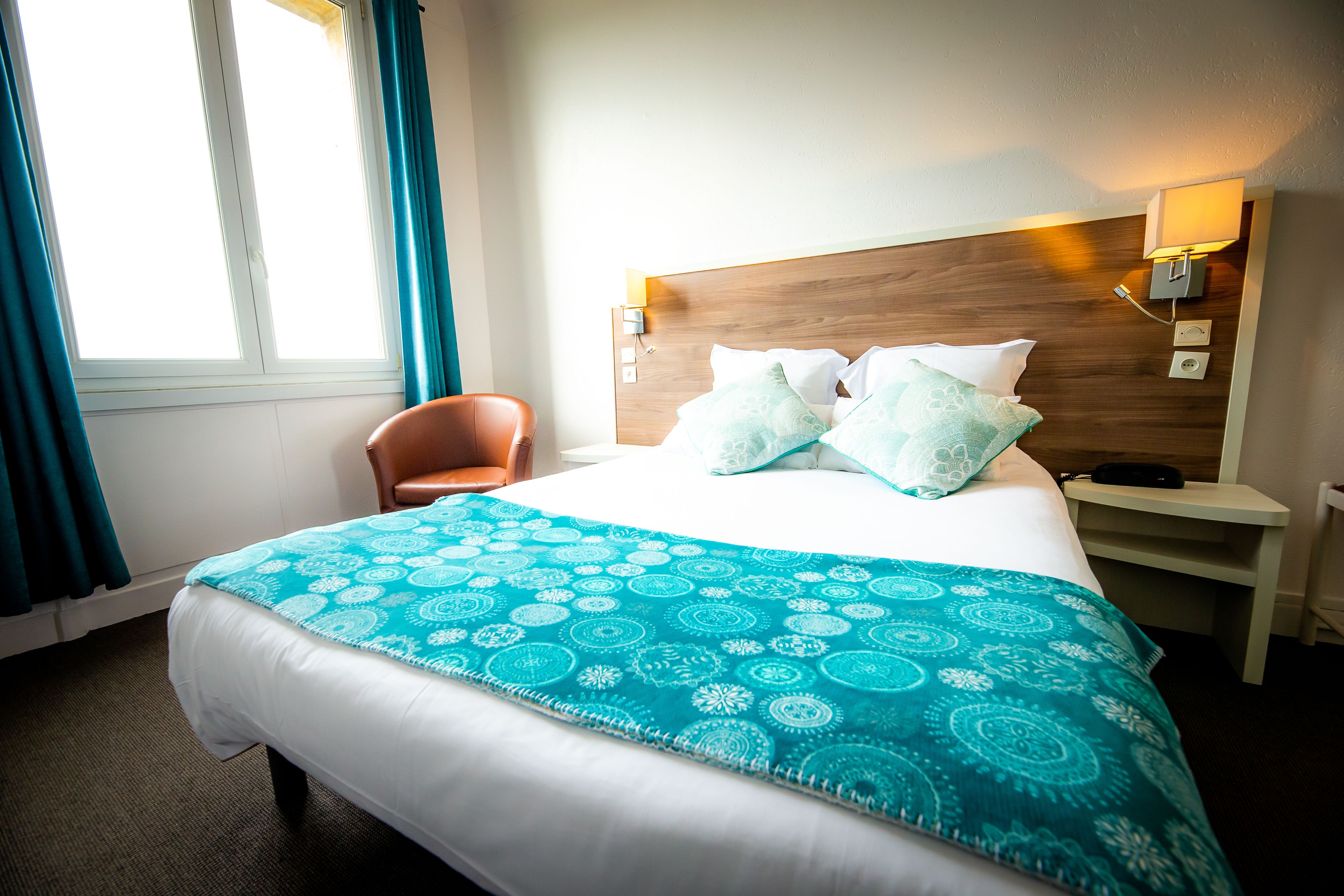 A hotel room with a large bed, a wooden headboard, a nightstand with a lamp, and a chair.